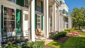 Eine Reihe weißer Gebäude im Kolonialstil mit grünen Fensterläden, eine Veranda mit Stühlen und ein gepflegter Garten mit Blumen und Sträuchern.
