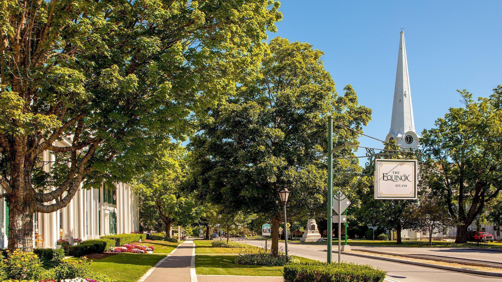 A tree-lined street with a church steeple and a sign for 'The Equinox' hotel.