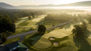 Vue aérienne d’un parcours de golf comportant plusieurs trous, des allées et une chaîne de montagnes en arrière-plan.