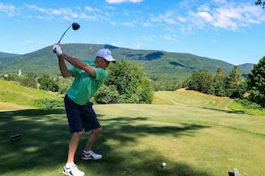 A golf course with a player in mid-swing, a flagstick, and a distant mountain. - Accessible Guest Room | King + Mountain View (Manchester)