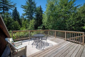 Eine Holzterrasse mit Tisch und Stühlen, umgeben von einem Geländer, und ein dichter Wald im Hintergrund.