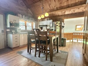 Ein Holzinnenraum mit Küche, Esstisch, Stühlen und einem kleinen Balkon.
