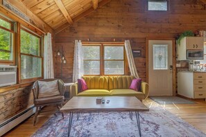 Ein gemütliches Blockhaus-Interieur mit Holzbalkendecke, einer Couch, einem Couchtisch und einer Küchenzeile mit Mikrowelle.