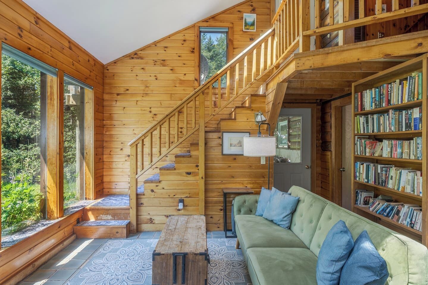 A wooden interior with a staircase, a green sofa, and a bookshelf.