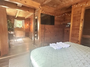 Ein Zimmer mit Holzboden, einem Bett, einem Fernseher und einem Fenster.