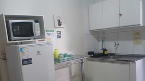A compact kitchen with a microwave, refrigerator, sink, and a small stool.