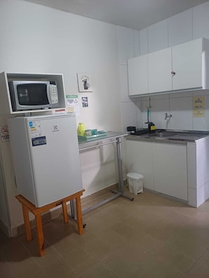 Une cuisine compacte équipée d’un four à micro-ondes, d’un réfrigérateur, d’un évier et d’un petit tabouret.