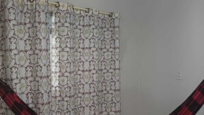 A room with a patterned curtain, a red and black checkered hammock, and tiled flooring.