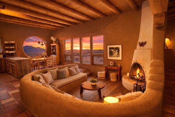 Ein gemütliches Wohnzimmer mit Kamin, einer runden Sitzecke und großen Fenstern mit Sonnenuntergangsblick.