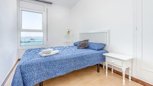 A bedroom with a bed, a bedside table, a radiator, a window with a view, and a small shelf with a plant. - Oceanfront House, BBQ, Central Location, Easy Parking, Wi-Fi, Very Spacious (Roses)