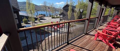 A wooden deck with red chairs, a view of a lake, and houses in the background.