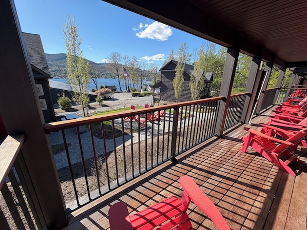 A wooden deck with red chairs, a view of a lake, and houses in the background.