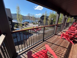 Une terrasse en bois avec des chaises rouges, une vue sur un lac et des maisons en arriĂšre-plan.