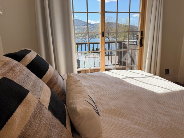 Une chambre avec une grande fenĂȘtre, un lit agrĂ©mentĂ© dâoreillers Ă rayures et une vue sur un balcon et des montagnes.