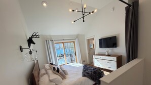 Ein Schlafzimmer mit Bett, Kommode, Fernseher und Fenster mit Blick.