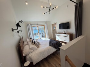 A bedroom with a bed, a dresser, a TV, and a window with a view.