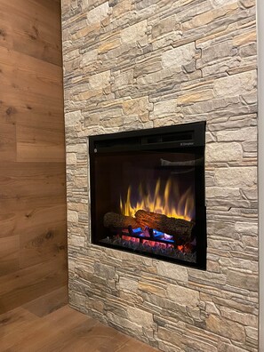 Ein Kamin mit Steinwand, Holzboden und schwarzem Rahmen.