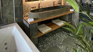 Un baño moderno con lavamanos de piedra, un espejo grande y una bañera.