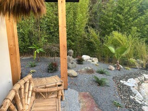 En træterrasse med en Buddha-statue, omgivet af en grussti, sten og forskellige planter.