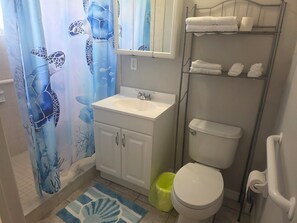 Ein Badezimmer mit weißem Waschbecken, Toilette, einer Duschvorhang mit Schildkrötenmotiv, einer kleinen Mülltonne und einem Regal mit Handtüchern.