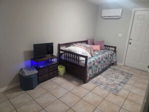 Ein Schlafzimmer mit einem Bett, einem Fernseher auf einem Schrank, einer Mülltonne und einer Klimaanlage an der Wand.
