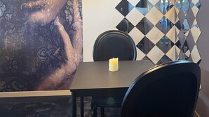 Een eetruimte met een tafel, stoelen, een kaars, een hanglamp en een muur met een geometrisch patroon.