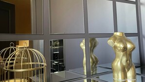 Een modern interieur met een spiegelende vloer, een hanglamp en een presentatie van gouden sculpturen.
