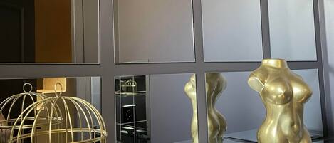 Un interno moderno con un pavimento riflettente, una lampada a sospensione e una vetrina di sculture dorate.