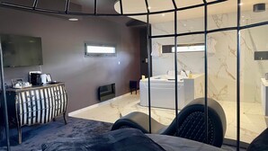 Een moderne hotelkamer met een bed, een bureau, een televisie, een badkamer met een wastafel en spiegel, en een groot raam.