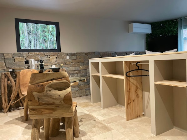 Une pièce avec un mur en pierre, une table en bois surmontée d’une vitre et un téléviseur fixé au mur.