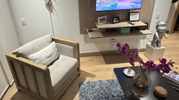 Un saló modern amb un sofà, un televisor fixat a la paret, un escriptori amb un ordinador i objectes decoratius.