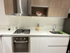 A modern kitchen with a gas stove, oven, sink, and wooden cabinets. - Alcalá Park - Cedritos, Bogotá (Bogotá)