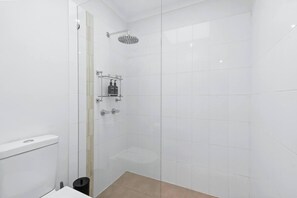 Um chuveiro moderno com porta de vidro, parede com azulejos brancos e um nicho pequeno com artigos de higiene pessoal.
