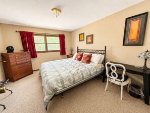 Een slaapkamer met een bed, een kaptafel, een bureau, een stoel en een raam met gordijnen.