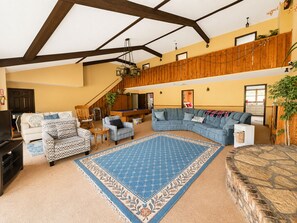 Een ruime woonkamer met een grote hoekbank, een pooltafel en een trap naar een hoger gelegen verdieping.
