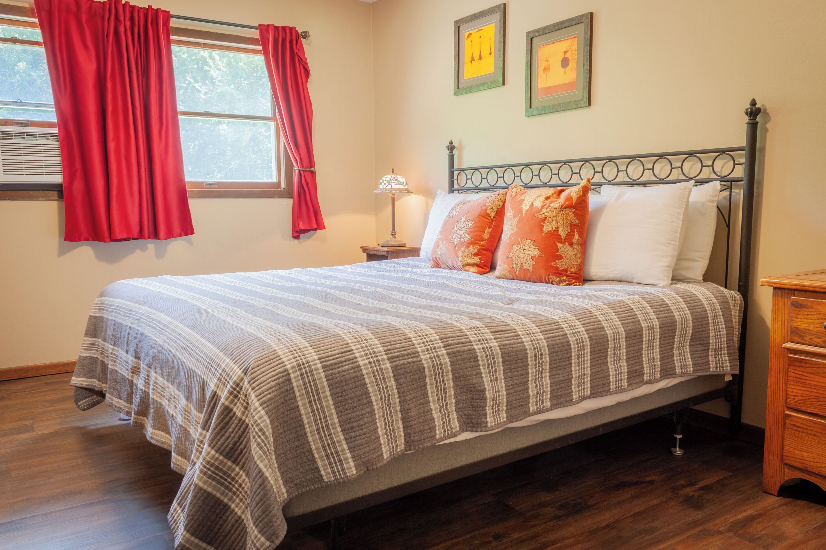 A neatly made bed with a plaid bedspread, a bedside table with a lamp, and two framed pictures on the wall.