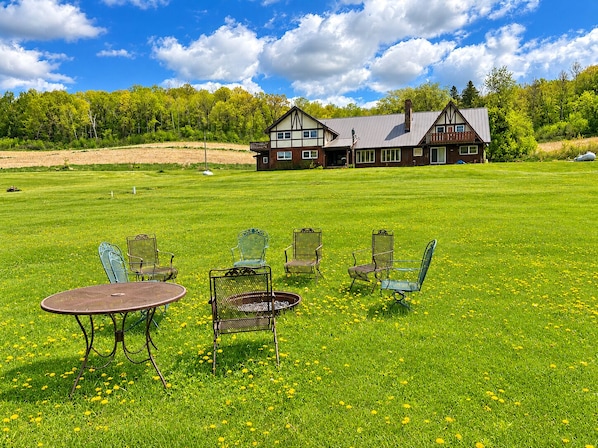 Une grande maison dotée d’une vaste pelouse, d’un espace extérieur aménagé pour s’asseoir et d’une vue sur la forêt environnante.