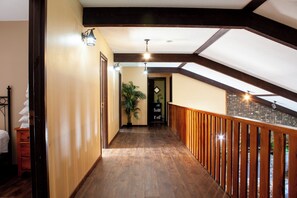 Un couloir en bois avec un plafond en pente, une rambarde en bois et une plante en pot.