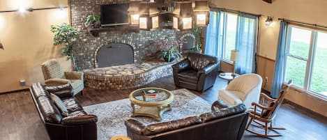 A spacious living room with a stone fireplace, leather furniture, and a large window providing natural light.