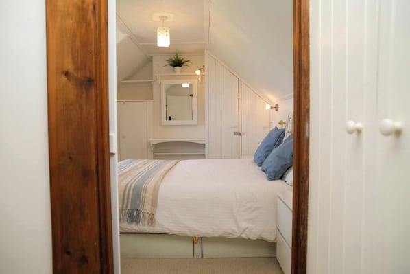 Ein Schlafzimmer mit einem Bett, einem Nachttisch, einer Kommode, einem Spiegel und einer Topfpflanze.