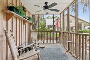 Eine überdachte Veranda mit Holzbalkonen, Deckenventilator und Gartenmöbeln.