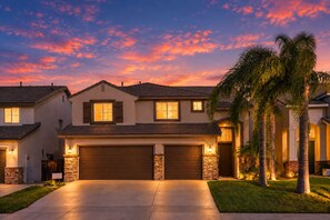 A two-story house with a garage, stone foundation, and a well-lit driveway.