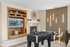 Een woonkamer met een televisie, open haard en een tafelvoetbaltafel.