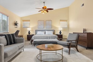 A hotel room with a bed, two bedside tables, a desk, a chair, a sofa, and a ceiling fan.