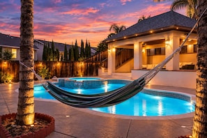 Ein Swimmingpool mit einer Hängematte, umgeben von einem Holzzaun, und ein Haus mit einer überdachten Terrasse.