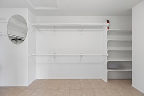 Ein Zimmer mit weißer Wand, einem runden Spiegel, einem weißen Regal und einem Fliesenboden.