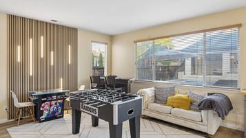 A room with a foosball table, a sofa, a window with blinds, and a wall with vertical slats.