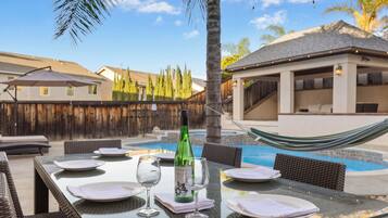 An outdoor dining area with a pool, dining tables, chairs, and a hammock.