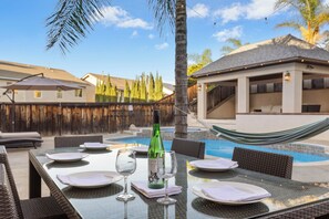 An outdoor dining area with a pool, dining tables, chairs, and a hammock.