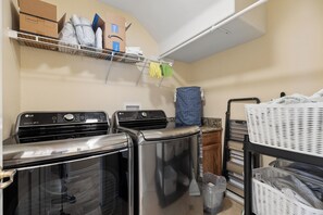 A laundry area with two dryers, a washing machine, and a shelf with folded clothes and boxes.